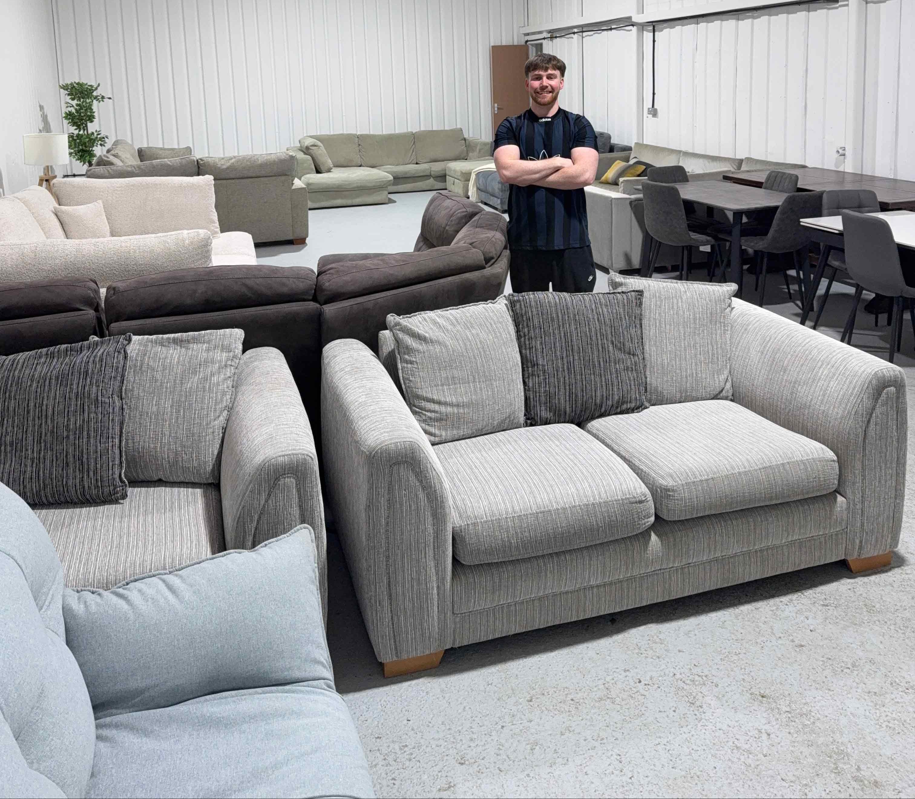 Man standing in a warehouse with various sofas and tables.